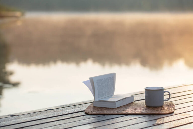 A book and coffee sitting out in front of a lake during a digital detox retreat